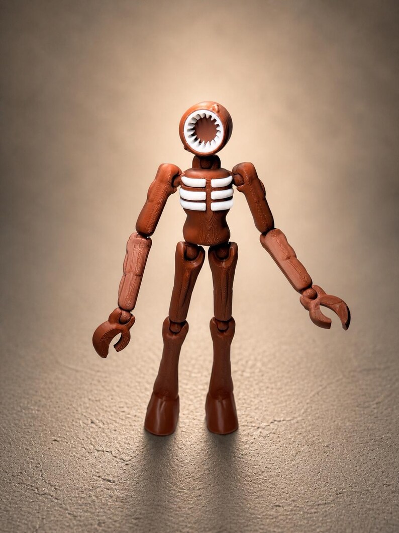 May include: A brown articulated figure with a circular head featuring a toothed mouth and a white interior. The figure has a rib cage design and claw-like hands. The figure is standing on a textured surface.