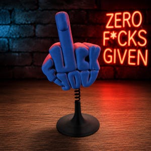 May include: A blue hand sculpture displaying a middle finger gesture, with the words FUCK YOU molded into the fingers. The sculpture is mounted on a black metal spring and a circular base. In the background, a red neon sign reads ZERO F*CKS GIVEN.