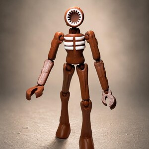May include: A brown Siren Head action figure with a speaker-like head and articulated limbs. The figure has white rib detailing and claw-like hands, standing on a neutral background. The toy is a collectible item.