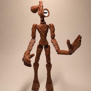 Puede incluir: Figura de acci&oacute;n de Siren Head marr&oacute;n con articulaciones. La figura tiene una cabeza con forma de altavoz con boca blanca y un cuerpo delgado y texturizado. Los brazos est&aacute;n extendidos y la figura se apoya en dos piernas con forma de tronco de &aacute;rbol.