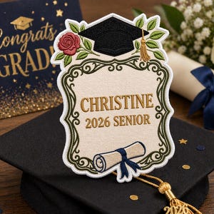 May include: A graduation-themed patch with the name "Christine" and "2026 Senior" embroidered on it. The patch features a black graduation cap, a red rose, and a scroll. A gold tassel with "2026" hangs below. A graduation card with "Congrats GRAD" is in the background.