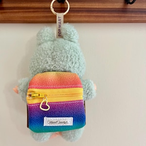 Peut inclure: Un porte-clés ours en peluche vert clair avec un sac à dos arc-en-ciel. Le sac à dos a une fermeture éclair dorée et un fermoir en forme de cœur. L'étiquette indique "POP MART" et le sac à dos dit "hand made".