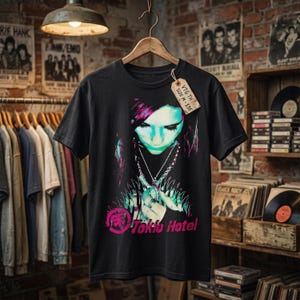 May include: A black short-sleeve t-shirt featuring a graphic print of a person with dark hair and teal-toned skin, wearing a chain necklace. The text 'Tokio Hotel' appears in pink below the graphic, and a cardboard tag reads 'VTG TH SIZE M-$35'.