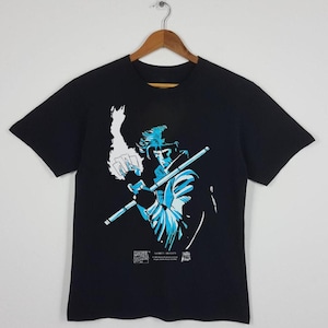 May include: Black t-shirt featuring a blue and white illustration of a comic book character holding a staff. The graphic includes the text "Gambit" and "Marvel Comics". The shirt is hanging on a wooden hanger.