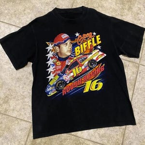 May include: Black t-shirt with a graphic of Greg Biffle and his #16 Roush Racing car. The design includes the text "Greg Biffle" and "Roush Racing 16" in yellow and red. The shirt has a crew neck and short sleeves. The image is a vintage style.