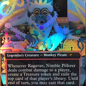 May include: A holographic Magic: The Gathering trading card titled Ragavan, Nimble Pilferer. The card features a stylized monkey pirate illustration, the text Legendary Creature - Monkey Pirate, and game rules text with a power and toughness of 2/1.