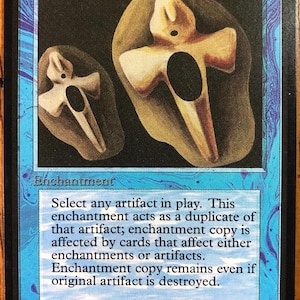 May include: A blue Magic: The Gathering trading card titled Copy Artifact. The card features an illustration of two tan, cross-shaped objects on a dark background. The text box explains the enchantment rules, and the artist credit is Amy Weber.