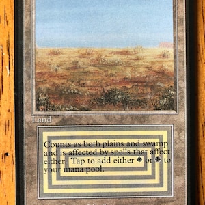 May include: A Magic: The Gathering card titled "Scrubland." The card features a landscape illustration of a dry, scrubby field under a blue sky. Text at the bottom describes its game function. The artist is Jesper Myrfors.