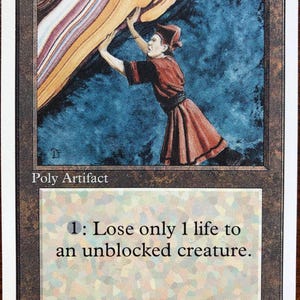 Peut inclure: Une carte à collectionner rectangulaire intitulée Forcefield avec une bordure brune et des bords blancs. L'illustration montre un personnage en tunique rouge poussant contre une barrière d'énergie multicolore. Le texte indique Poly Artifact et 1: Lose only 1 life to an unblocked creature. Illus. Dan Frazier.