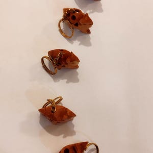 Op de afbeelding: Een verzameling kleine, gesneden houten sleutelhangers in de vorm van gestileerde dieren. De sleutelhangers zijn warmbruin met goudkleurige sleutelringen. Sommige hebben donkerbruine vlekken.