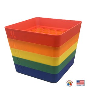 May include: A rainbow-colored, tiered storage container with sizes labeled XL, L, M, S, and XS. The container is made of plastic and has a honeycomb-patterned top. The bottom right corner shows a logo and a "Made in USA" sticker.