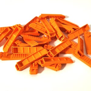 May include: A pile of bright orange plastic shims, of various shapes and sizes, are scattered on a white surface. The shims appear to be new and unused, with a clean, smooth texture. The image is well-lit, highlighting the vibrant color and details.