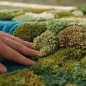 May include: Close-up of a textured rug with a tufted design. The rug features a pattern of green, brown, and blue tufts, creating a soft, tactile surface. The color palette evokes a natural, earthy feel.