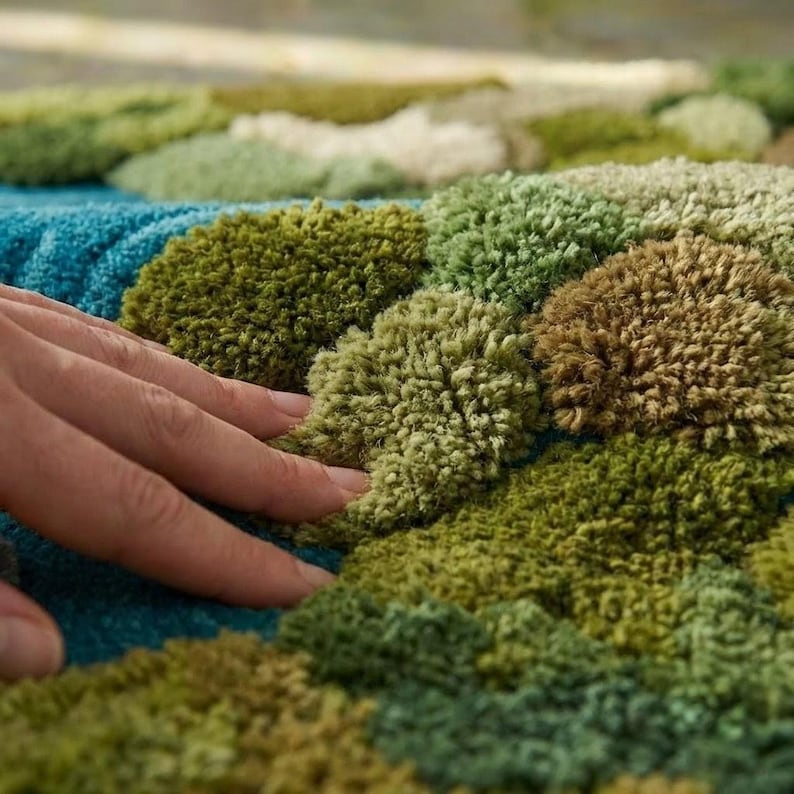May include: Close-up of a textured rug with a tufted design. The rug features a pattern of green, brown, and blue tufts, creating a soft, tactile surface. The color palette evokes a natural, earthy feel.