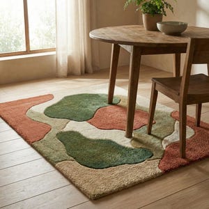 Puede incluir: Una alfombra rectangular con un dise&ntilde;o abstracto en tonos verdes, &oacute;xido y beige. La alfombra est&aacute; colocada sobre un suelo de madera debajo de una mesa y una silla de madera. El dise&ntilde;o de la alfombra presenta formas org&aacute;nicas.