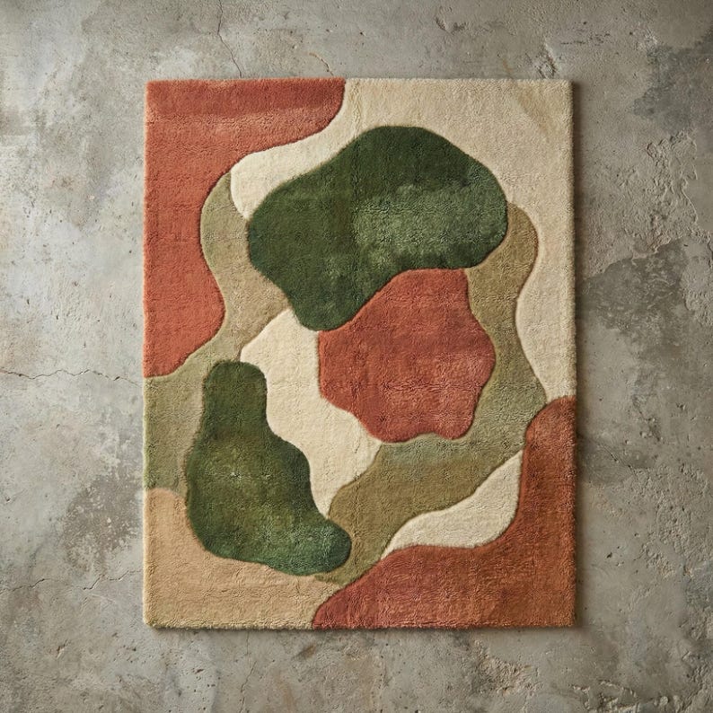 Puede incluir: Una alfombra rectangular con un dise&ntilde;o abstracto. La alfombra presenta formas org&aacute;nicas en tonos de verde, &oacute;xido, beige y marr&oacute;n. La alfombra est&aacute; hecha de un material suave y texturizado y est&aacute; colocada sobre un suelo de hormig&oacute;n.