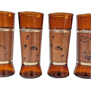 May include: Set of four amber glass drinking glasses with a woodgrain design and black markings. Each glass has a gold band around the middle.