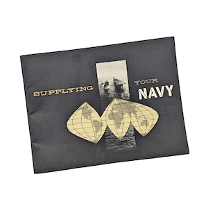 May include: A dark gray brochure with gold lettering that reads "SUPPLYING YOUR NAVY." The brochure features a black and white image of naval ships and three stylized world map graphics.