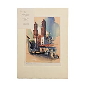 May include: A vintage print of a church with two tall towers, a dome, and a red-tiled roof. The artwork is in a watercolor style, with soft colors and a serene atmosphere. The print includes text that reads "Wishing you a Merry Christmas and a Happy New Year."