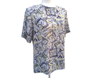 May include: A short-sleeved top with a geometric pattern in shades of blue, yellow, green, and gray. The pattern features abstract shapes and lines. The top is displayed on a mannequin.