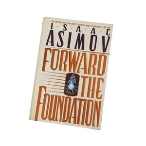 Puede incluir: Un libro de tapa dura titulado "FORWARD THE FOUNDATION" de Isaac Asimov. La portada es de color blanquecino con letras naranjas. El título del libro se muestra de forma destacada, con el nombre del autor en la parte superior. Una pequeña ilustración de una figura está en el centro.