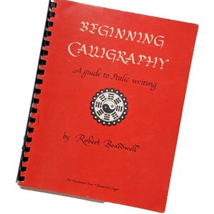 May include: Red book with a black spiral binding titled "BEGINNING CALLIGRAPHY A guide to Italic writing by Robert Boardwell" with a black and white yin yang symbol in a circle on the cover.
