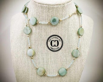May include: A necklace with large, round, pale green beads interspersed with smaller, clear beads and gold-colored accents. The necklace is displayed on a mannequin. The logo "Creations by Christine" is visible.
