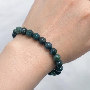 Könnte beinhalten: Ein Armband mit runden Perlen in Dunkelgrün und Türkis. Das Armband wird am Handgelenk getragen und zeigt die Farbvariationen und die glatte Textur der Natursteinperlen. Die Perlen haben einen Durchmesser von etwa 0,8 cm.
