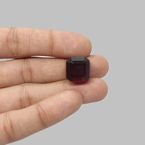 Könnte beinhalten: Ein dunkelbrauner, rechteckiger Edelstein mit Smaragdschliff. Der Stein hat mehrere Facetten und wird in einer Hand gehalten. Der Hintergrund ist ein neutrales Grau. Der Edelstein ist wahrscheinlich ein Schmuckstein.