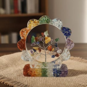 Könnte beinhalten: Eine dekorative Baumskulptur mit einem klaren, kreisförmigen Rahmen und einem Regenbogenfarbenen Sockel. Der Baum hat einen Drahtstamm und bunte Edelsteinblätter. Der Rahmen ist von einem wellenförmigen Rand aus verschiedenfarbigen Steinen umgeben.