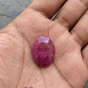 Könnte beinhalten: Ein ovaler, facettierter Edelstein in einem tiefen Magenta- und Rosaton. Der Stein hat eine polierte Oberfläche mit mehreren geometrischen Facetten, die das Licht reflektieren und eine durchscheinende Qualität sowie eine satte Farbe zeigen.
