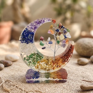 Könnte beinhalten: Eine dekorative Halbmondskulptur mit einem farbenfrohen, geschichteten Design. Der Mond ist mit verschiedenfarbigen Steinen gefüllt, darunter Lila, Blau, Grün, Gelb, Orange und Rot. In der Mitte befindet sich ein kleiner Drahtbaum mit bunten Steinen.