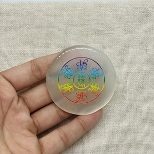 Könnte beinhalten: Ein klarer, runder Stein mit einem Regenbogen-Design. Das Design enthält Symbole und die Zahlen 808, 520 und 741. Der Stein wird in einer Hand gehalten.