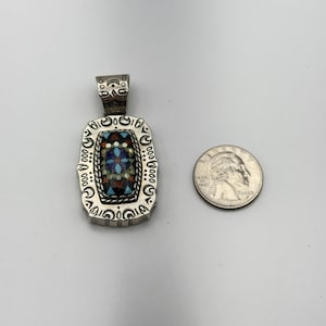 May include: Silver rectangular pendant with a mosaic design of blue, red, and white stones. The pendant has a decorative border and a loop for a chain. A coin is next to the pendant for size comparison.