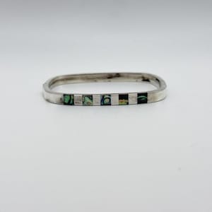May include: A silver-toned, rectangular bangle bracelet. The bracelet features inlaid rectangular sections of iridescent abalone shell and silver. The bracelet is displayed on a white background.