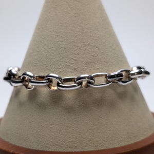 May include: A silver-toned chain bracelet featuring a series of interconnected oval links. The metal has a polished, reflective surface, and the links are uniform in size and shape, creating a continuous, flexible band design.