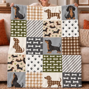 Puede incluir: Una manta suave con un diseño de patchwork de perros salchicha, patrones de cuadros marrones y blancos, rayas diagonales y motivos repetidos de huesos y huellas. La manta muestra varias ilustraciones de perros salchicha negros y fuego.