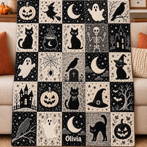 May include: A black and white quilt featuring a grid of squares with Halloween-themed illustrations including pumpkins, black cats, ghosts, witches, skeletons, ravens, and a haunted house. The name Olivia is printed in white on one of the squares.