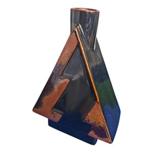 Peut inclure: Un vase géométrique en céramique avec un design triangulaire. Le vase présente une palette de couleurs marron foncé et noire avec des accents cuivrés. Le vase a une forme unique et une finition brillante.