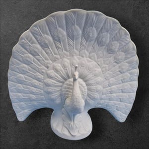 May include: A white ceramic peacock sculpture with a fanned tail. The peacock is centered on a round base, with detailed feather patterns. The sculpture is set against a dark grey background.