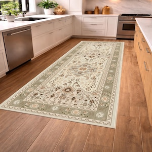 May include: A rectangular area rug with an intricate floral pattern in beige, brown, and green tones. The rug has a border with a repeating floral design and is placed on a hardwood floor in a kitchen setting.