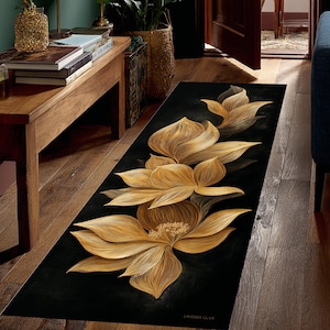 May include: A long, black rug with a gold and tan floral design. The flowers are stylized with detailed petal patterns. The rug is placed on a wooden floor. The rug's design is reminiscent of a lotus flower.