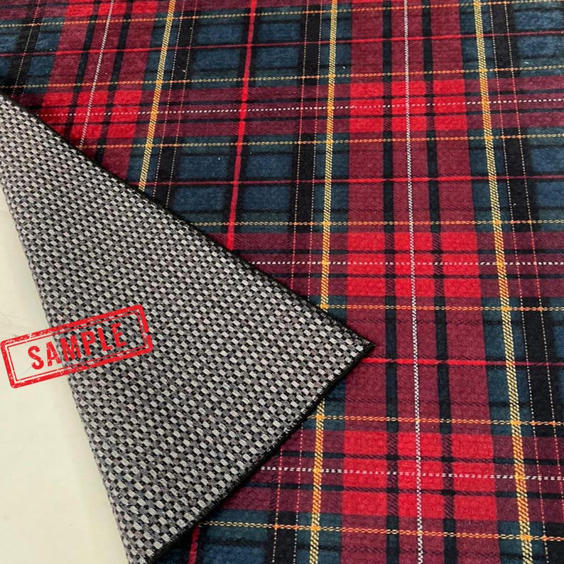 May include: A close-up of a plaid fabric with a red, blue, and yellow pattern. The fabric is folded over, revealing a gray and white checkered underside. The word "SAMPLE" is stamped on the fabric.