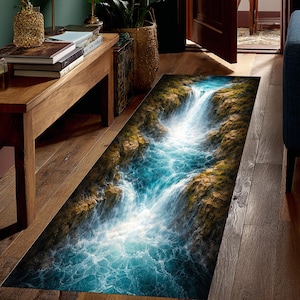 Op de afbeelding: Een rechthoekig tapijt met een watervalscène. Het ontwerp toont een waterval met turquoise water en rotsachtige kliffen, wat een realistisch visueel effect creëert. Het tapijt is ontworpen voor gebruik binnenshuis.
