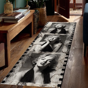 May include: A rectangular runner rug featuring three black and white images of Marilyn Monroe. The images are set against a distressed, cracked background, framed by a black border. The rug is placed on a wooden floor.