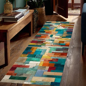 Könnte beinhalten: Ein rechteckiger Teppich mit einem farbenfrohen, abstrakten Design. Der Teppich weist ein Muster aus rechteckigen Blöcken in Blau-, Türkis-, Orange-, Rot-, Gelb- und Beigetönen auf. Der Teppich liegt auf einem Holzboden und verleiht dem Raum eine lebendige Note.