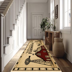 May include: A rectangular runner rug featuring a cream-colored background with a black border. The design includes a red barn, a black windmill, and a rooster graphic. The text "Welcome to our FARMHOUSE" is printed in black script and block lettering.