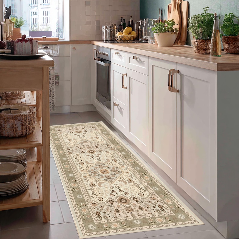 May include: A rectangular beige kitchen rug with an intricate floral pattern and a sage green border. The rug is placed in front of white cabinets and a stove, adding a decorative element to the kitchen.