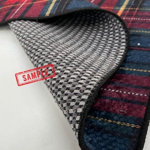 May include: Close-up of a plaid fabric with a gray and white patterned underside. The plaid features red, blue, and yellow stripes. The word "SAMPLE" is stamped in red on the gray side.