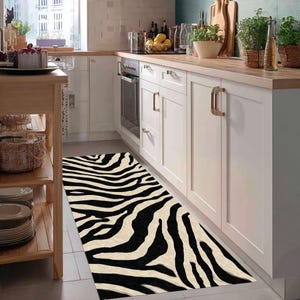 Puede incluir: Una alfombra de pasillo con estampado de cebra en blanco y negro en una cocina. El patrón de la alfombra es un diseño audaz y repetitivo de rayas negras sobre un fondo crema. La alfombra rectangular está colocada sobre un suelo embaldosado.